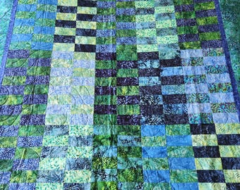May include: A handmade quilt with a patchwork design in shades of blue and green. The quilt features a variety of patterned fabrics, creating a visually interesting and textured surface. The border is a darker shade of blue, and the quilt is likely queen or king size.