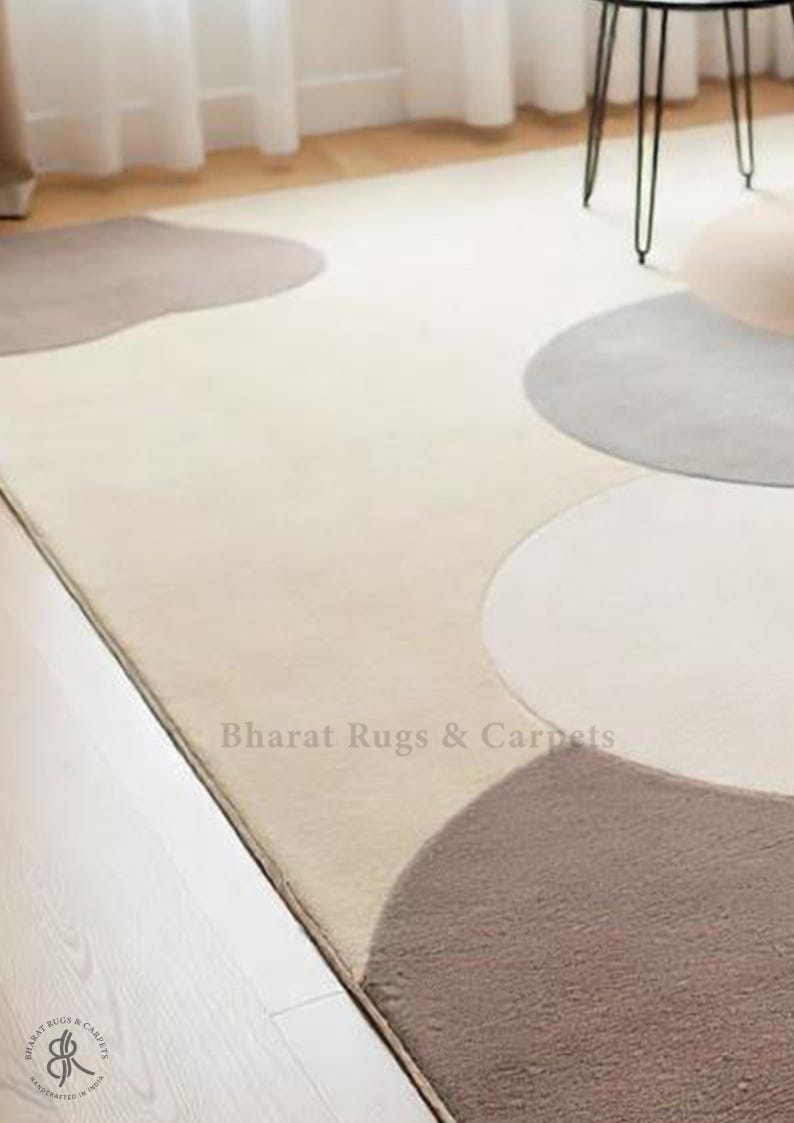 May include: A cream-colored rug with a modern design featuring overlapping circles in shades of gray and brown. The rug is made of soft, plush material and has a subtle sheen. The text "Bharat Rugs & Carpets" is visible in the lower right corner of the rug.