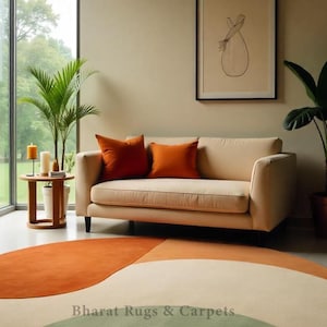 Puede incluir: Una alfombra redonda multicolor con un esquema de color verde, crema, naranja y &oacute;xido. La alfombra est&aacute; en un sal&oacute;n con un sof&aacute; blanco y almohadas naranjas. El texto "Bharat Rugs & Carpets" es visible en la alfombra.