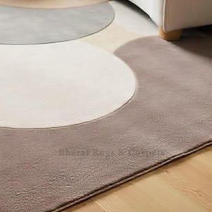 May include: A modern abstract rug with a design of overlapping circles in shades of beige, gray, and brown. The rug has a soft, plush texture and a subtle sheen.