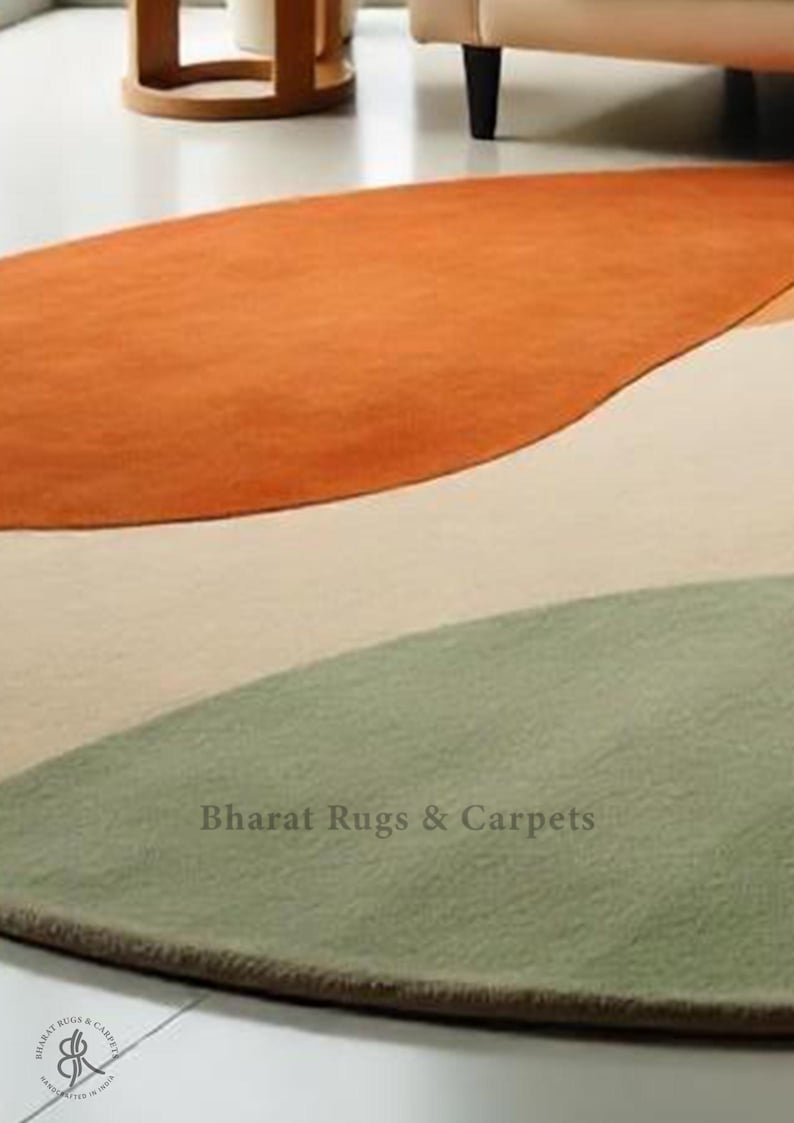 Puede incluir: Una alfombra redonda abstracta en tres colores: naranja, beige y verde. La alfombra tiene una forma ondulada org&aacute;nica y una textura sutil. El texto "Bharat Rugs & Carpets" est&aacute; impreso en la alfombra.