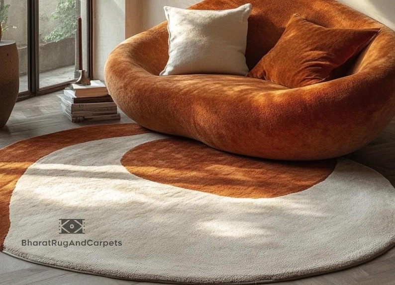 May include: A round, cream-colored rug with two concentric brown circles. The rug is in front of a large, orange, plush sofa with two pillows.