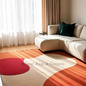 May include: A rectangular area rug featuring a large-scale abstract pattern with bold, curved shapes in solid red, burnt orange, and cream. The text Bharat Rugs & Carpets is printed in the center of the rug, which is placed on a light wood floor.