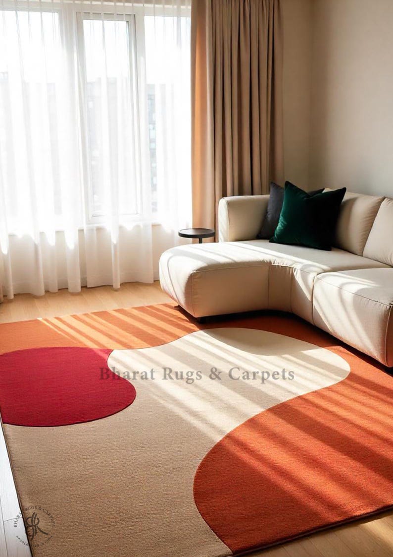 May include: A rectangular area rug featuring a large-scale abstract pattern with bold, curved shapes in solid red, burnt orange, and cream. The text Bharat Rugs & Carpets is printed in the center of the rug, which is placed on a light wood floor.