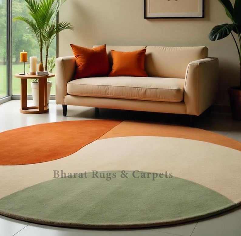 Puede incluir: Una alfombra redonda multicolor con un esquema de colores verde, crema, naranja y &oacute;xido. La alfombra est&aacute; en un sal&oacute;n con un sof&aacute; de color crema y una peque&ntilde;a mesa auxiliar de madera.