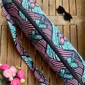 Könnte beinhalten: Ein schwarzer Yogamatte-Tragebeutel mit einem geometrischen Muster in Pink und Blau. Der Beutel hat einen Reißverschluss und einen langen Riemen. Der Riemen ist ebenfalls mit dem gleichen geometrischen Muster in Pink und Blau verziert. Der Beutel hat ein kleines braunes Etikett mit dem Text "HAND MADE" darauf.