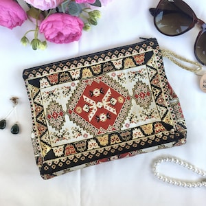 May include: A black and gold clutch purse with a red, white, and gold patterned design. The pattern resembles a traditional rug or tapestry.