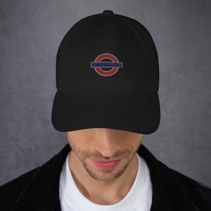 May include: Black baseball cap with a red and blue embroidered logo. The logo is a circle with a horizontal bar through the center. The cap has a curved brim and a fabric strap closure.