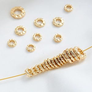 Puede incluir: Una colección de anillos de metal dorado con una superficie texturizada. Los anillos están dispuestos en una pila y sobre una superficie blanca.