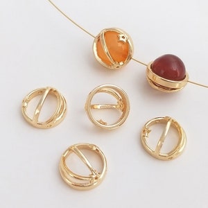 May include: Five gold-toned metal beads with a star design. Two beads have a clear orange center and two beads have a clear red center. One bead is a plain gold-toned ring.