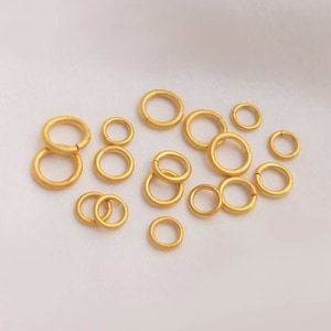 May include: A collection of gold-toned jump rings in various sizes. The jump rings are smooth and have a matte finish.