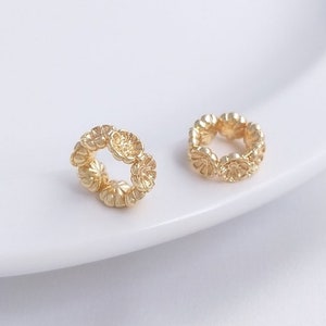 May include: Two gold-colored metal rings with a decorative floral design. Each ring is made up of small, round, flower-shaped pieces.