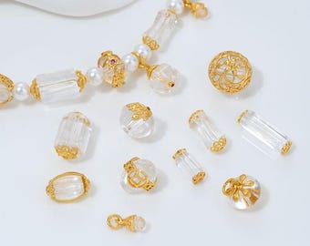 May include: A collection of clear, faceted beads with gold-colored accents and a pearl necklace. The beads vary in shape, including round, oval, and cylindrical. The gold accents feature intricate filigree designs, creating an elegant aesthetic.