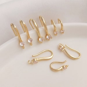 Puede incluir: Un conjunto de ganchos para pendientes de color dorado con detalles de cristal transparente. Los ganchos están disponibles en diferentes estilos, incluyendo un bucle simple y un diseño más elaborado con un gancho curvo.