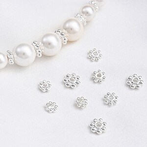 May include: A set of silver-toned bead caps with a flower design. The bead caps are arranged on a white surface.