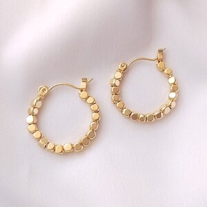 May include: A pair of gold hoop earrings with a beaded design. Each earring is made up of small, round, gold beads.
