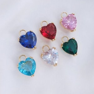 May include: Six heart-shaped charms with different colored rhinestones. The charms are gold-toned and have a loop at the top for attaching to a necklace or bracelet. The colors of the rhinestones are pink, red, blue, green, clear, and light blue.