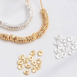 Könnte beinhalten: Zwei Halsketten aus goldenen und silbernen Metallringen. Die Halsketten werden auf einer weißen Oberfläche mit losen goldenen und silbernen Ringen präsentiert.