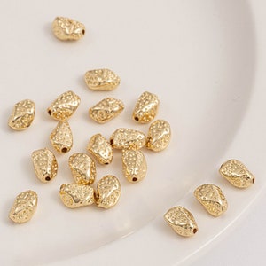 Könnte beinhalten: Eine Sammlung goldfarbener Metallperlen mit einer strukturierten Oberfläche. Die Perlen sind oval geformt und haben ein Loch in der Mitte zum Auf fädeln.
