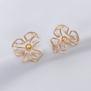 May include: A pair of gold-tone flower-shaped earrings with clear crystal accents.