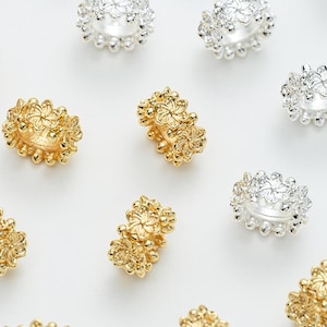 Può includere: Una collezione di anelli in oro e argento con intricati disegni floreali. Gli anelli sono disposti su uno sfondo bianco.