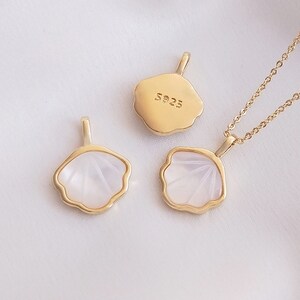 May include: Gold-toned pendant necklaces and charms with a seashell design. The pendants have a white, fan-shaped inlay and are attached to a delicate chain. One pendant has "S925" stamped on the back.