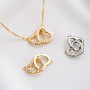 Puede incluir: Dos collares de tono dorado con colgantes de corazón entrelazados. Los corazones están adornados con piedras de circonita cúbica transparentes.