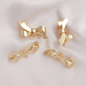 May include: Four gold-toned bow-shaped brooches. Two of the brooches are simple bows, while the other two are more ornate with a swirl design.