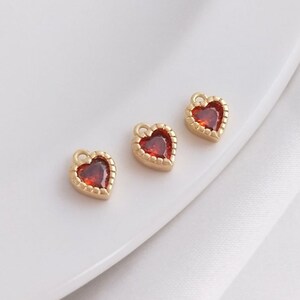 Puede incluir: Tres abalorios dorados en forma de coraz&oacute;n con detalles de gemas rojas. Los abalorios tienen un borde de cuentas y un bucle para sujetarlos a joyas.
