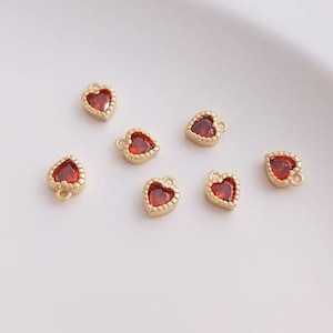Puede incluir: Siete abalorios dorados en forma de coraz&oacute;n con centros de pedrer&iacute;a roja. Los abalorios tienen un bucle en la parte superior para sujetarlos a joyas.