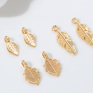May include: Gold-coloured leaf and feather charms. The charms have a loop at the top for attaching to jewellery. The leaves and feathers have detailed veining and texture. The charms are small and delicate, suitable for earrings or necklaces.