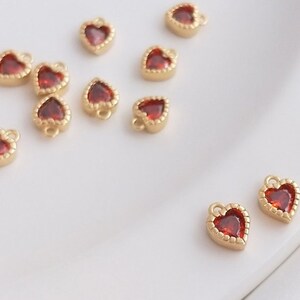Puede incluir: Una colecci&oacute;n de peque&ntilde;os abalorios de coraz&oacute;n de oro con acentos de gemas rojas. Los abalorios tienen un bucle en la parte superior para sujetarlos a joyas u otras manualidades.