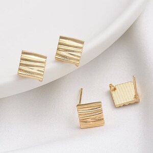 May include: Three gold-toned earring posts with square-shaped tops. The tops have a textured, ribbed design.