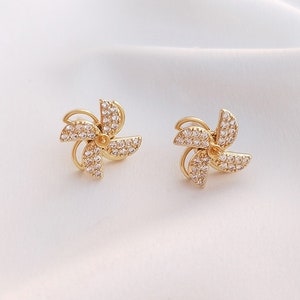 May include: A pair of gold earrings with a pinwheel design. Each earring is adorned with clear sparkling stones.