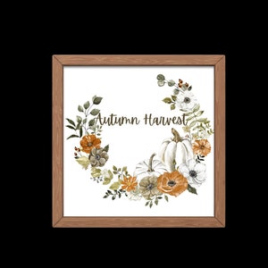 May include: Wooden framed print with a watercolour wreath of pumpkins, flowers, and foliage in orange, white, and green. The text "Autumn Harvest" is written in a script font.