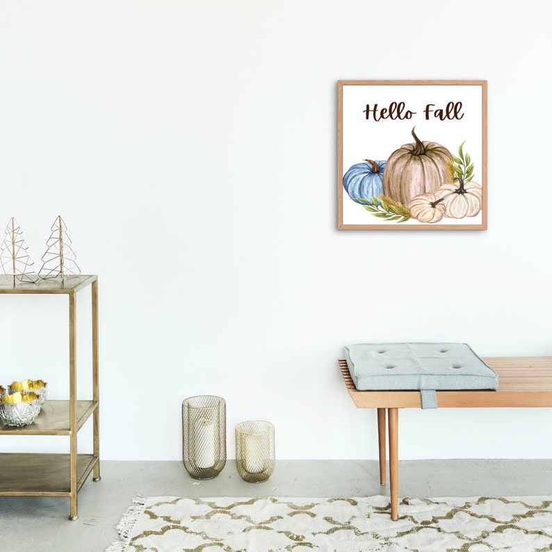 Op de afbeelding: Een ingelijst aquarel schilderij van pompoenen en pompoenen met de tekst "Hello Fall" in bruine letters. De pompoenen zijn wit, beige en blauw.