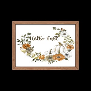 May include: A framed print with a white background featuring a watercolor illustration of a wreath of fall foliage, pumpkins, and flowers. The text "Hello Fall" is written in the center of the wreath.