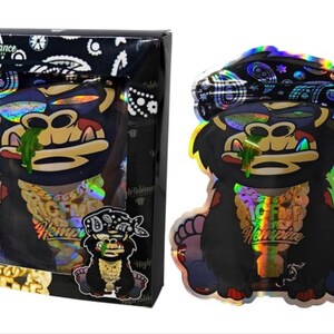 K&ouml;nnte beinhalten: Ein schwarzer und holografischer Gorilla-Aufkleber mit Bandana, goldener Kette und gr&uuml;nem Sabber. Der Aufkleber befindet sich in einer schwarzen Box mit den Worten "High Tolerance" und einer kleineren Gorilla-Grafik.