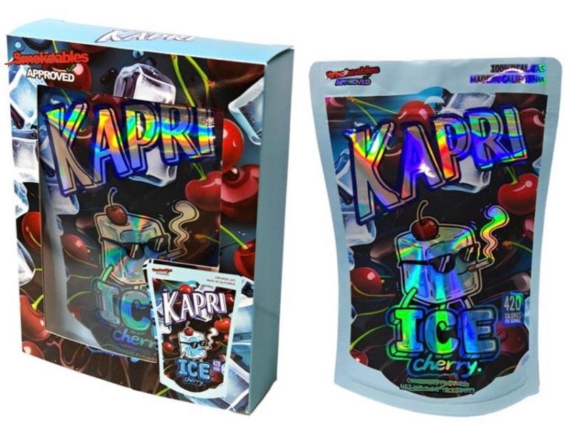 K&ouml;nnte beinhalten: Zwei Packungen "Kapri Ice Cherry" Produkte. Eine ist eine Box mit einem transparenten Fenster, die andere ein Beutel. Beide zeigen ein holografisches "Kapri"-Logo, Kirschillustrationen und den Text "Ice Cherry."