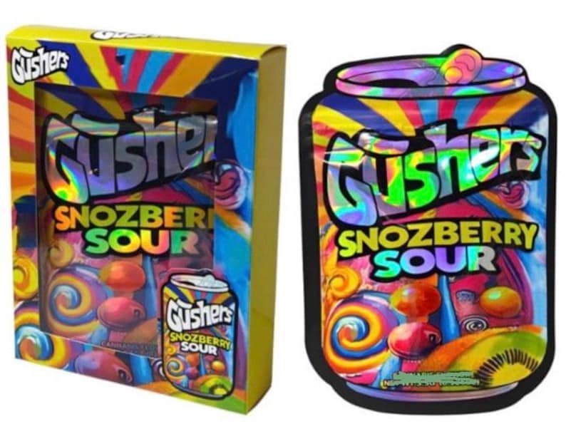 K&ouml;nnte beinhalten: Eine Schachtel und eine Dosen-Grafik von Gushers Snozberry Sour S&uuml;&szlig;igkeiten. Die Schachtel ist gelb mit einem farbenfrohen Design und dem Gushers-Logo. Die Dosen-Grafik zeigt das gleiche Logo und S&uuml;&szlig;igkeiten-Bilder mit einem lebendigen, regenbogenartigen Hintergrund.