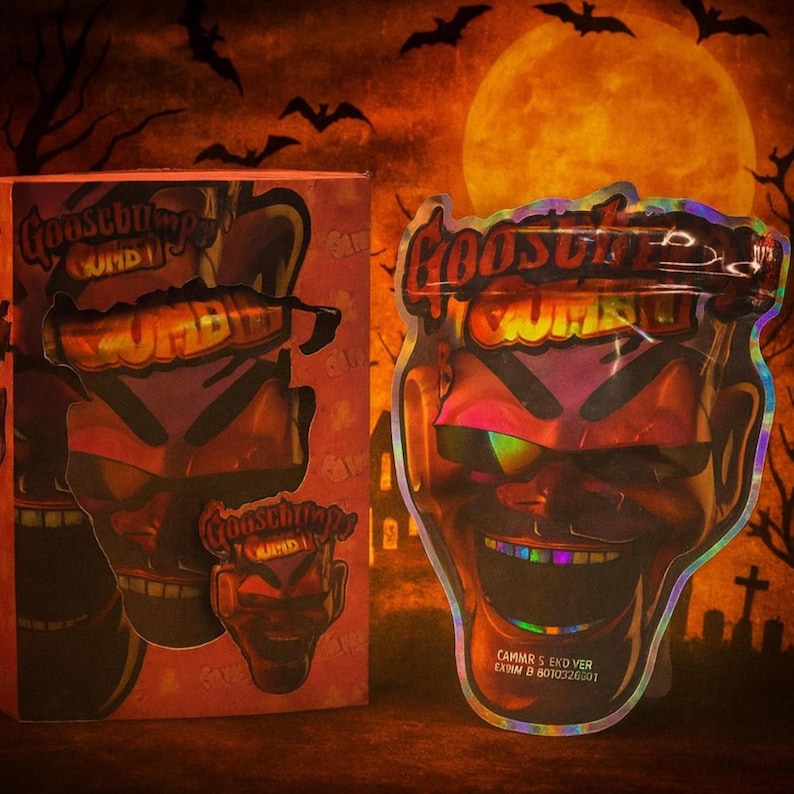 K&ouml;nnte beinhalten: Ein Halloween-Produkt mit dem Text "Goosebumps ZOMBIE". Das Bild zeigt eine rote Schachtel und einen holografischen Beutel in Form eines teuflischen Gesichts mit Regenbogenaugen und -z&auml;hnen. Der Hintergrund zeigt einen Vollmond, Flederm&auml;use und einen Friedhof.