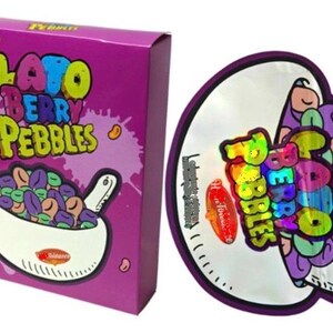 K&ouml;nnte beinhalten: Eine lila Schachtel und ein runder Aufkleber mit den Worten "Lato Berry Pebbles" in farbenfrohem Text. Die Schachtel zeigt eine Sch&uuml;ssel mit bunten Cerealien und der Aufkleber hat ein &auml;hnliches Design.
