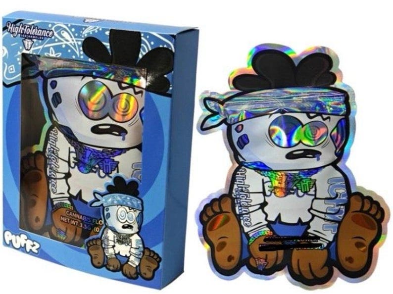 K&ouml;nnte beinhalten: Eine blaue Schachtel und ein holografischer Beutel mit einer Cartoonfigur mit blauem Bandana und braunen F&uuml;&szlig;en. Die Figur hat gro&szlig;e Augen und einen &uuml;berraschten Gesichtsausdruck. Auf der Schachtel steht "High Tolerance" und "PUFFz".