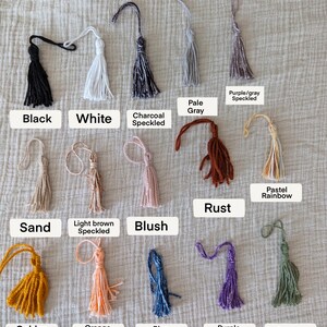 Peut inclure: Une collection de pompons faits &agrave; la main de diff&eacute;rentes couleurs, dont le noir, le blanc et des options mouchet&eacute;es. Chaque pompon est &eacute;tiquet&eacute; avec son nom de couleur, comme "Blush", "Rust" et "Golden Yellow". Les pompons sont pr&eacute;sent&eacute;s sur un tissu textur&eacute; de couleur neutre.