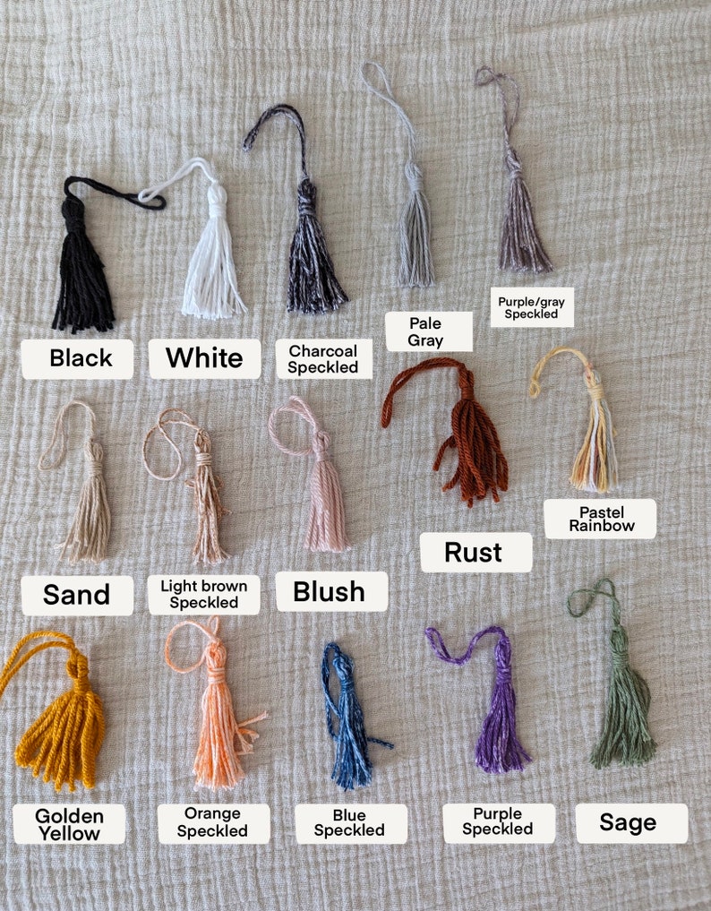 Peut inclure: Une collection de pompons faits &agrave; la main de diff&eacute;rentes couleurs, dont le noir, le blanc et des options mouchet&eacute;es. Chaque pompon est &eacute;tiquet&eacute; avec son nom de couleur, comme "Blush", "Rust" et "Golden Yellow". Les pompons sont pr&eacute;sent&eacute;s sur un tissu textur&eacute; de couleur neutre.