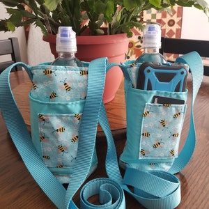 May include: Two turquoise blue water bottle holders with adjustable straps. Each holder features a bee and floral print and a pocket for a phone or other small items.