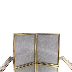 May include: A gold-toned, multi-panel picture frame with a textured gray backing. The frame has a decorative rope-like border. The frame is designed to hold multiple photos and is hinged to fold.