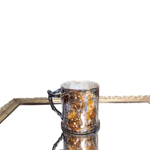 Könnte beinhalten: Eine Keramik-Tasse mit einer einzigartigen, strukturierten Oberfläche in Braun-, Gold- und Weißtönen. Der Griff hat ein dunkles, astähnliches Design. Die Tasse spiegelt sich in einer spiegelnden Oberfläche.