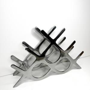 May include: A modern, silver-colored wine rack with a geometric design. The rack is made of metal and features multiple circular openings to hold wine bottles. The design is sleek and contemporary, suitable for home decor.