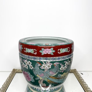 May include: A ceramic planter featuring a deep green background with colorful illustrations of birds perched on flowering branches. The rim is a wide band of dark red decorated with pink and blue floral motifs and white accents.